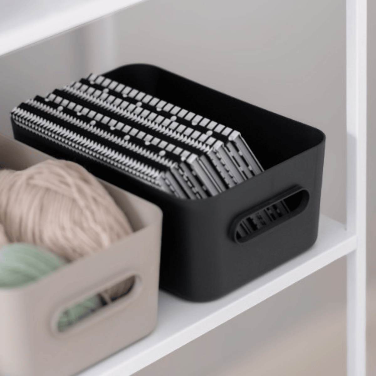 Koksgrå SmartStore Comfort oppbevaringskurv med strikkepinner ved siden av en beige kurv med garn