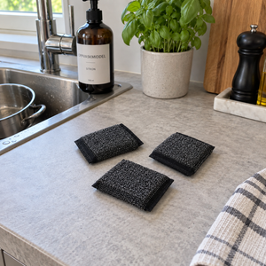 Tre svarte grytesvamper i rustfritt stål ligger på kjøkkenbenken ved vasken.