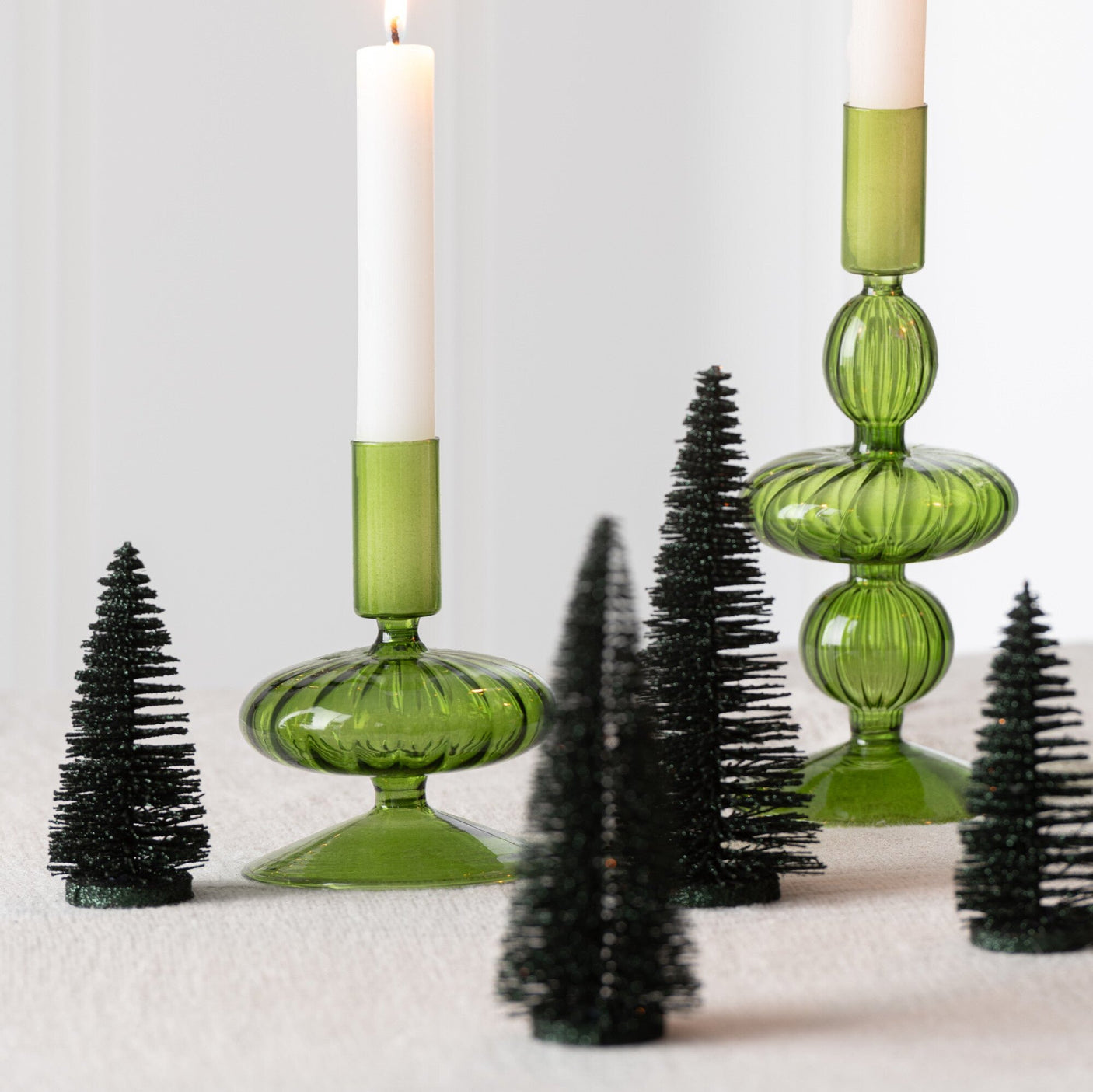 Pyntefat med mørkegrønne miniatyrjuletrær, nisser, lys og julekuler, stylet til jul med juletre i bakgrunnen.
