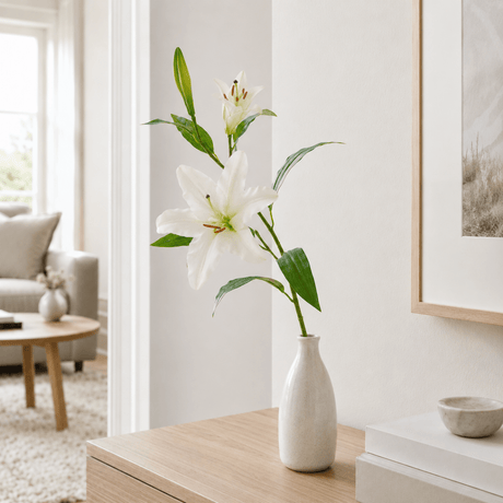 Kunstig hvid lilje med realistiske blomster og blade på grøn stilk. I en hvid keramikkvase i et nordisk hjem