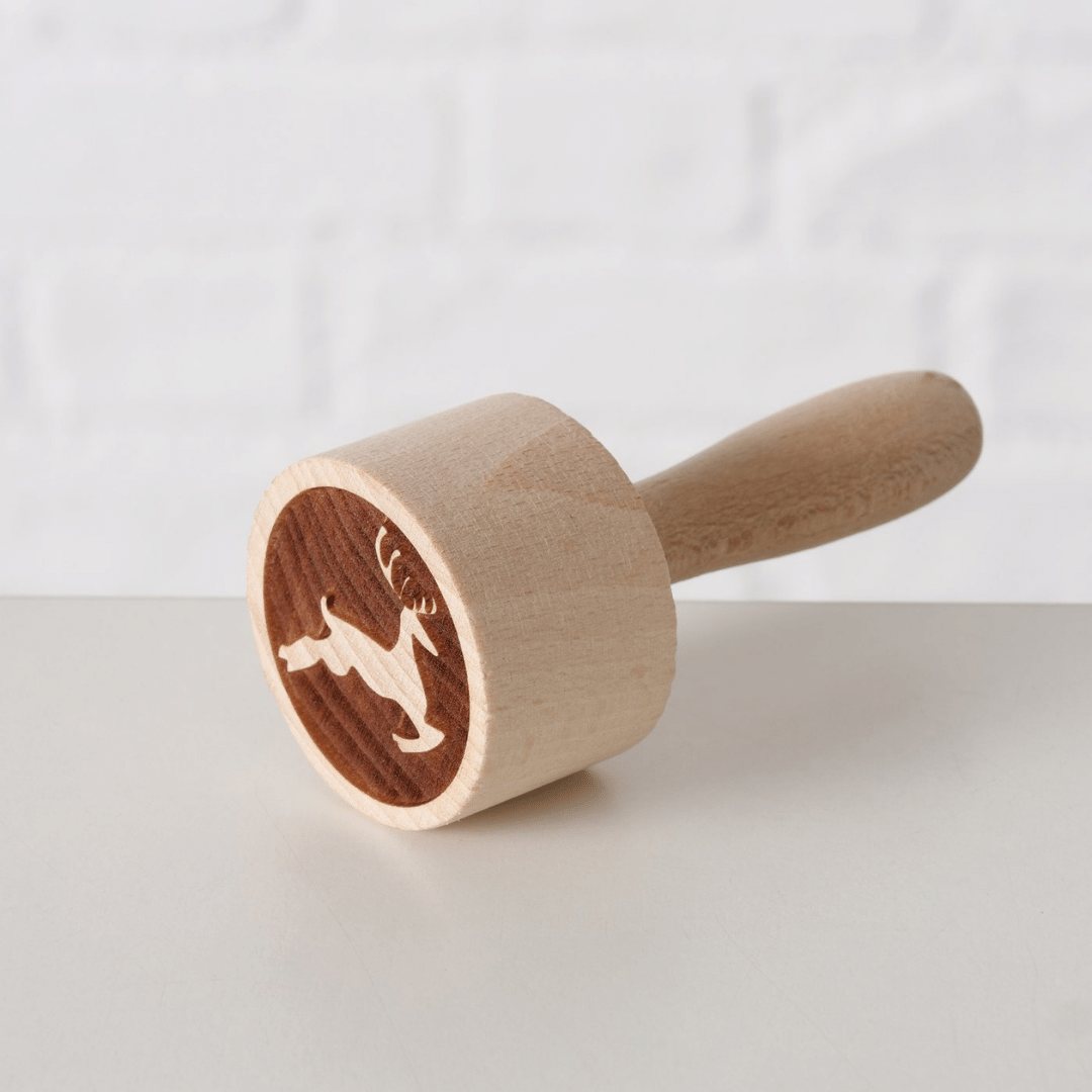 Kakestempel i tre med hoppende reinsdyr­motiv, liggende på lys overflate.