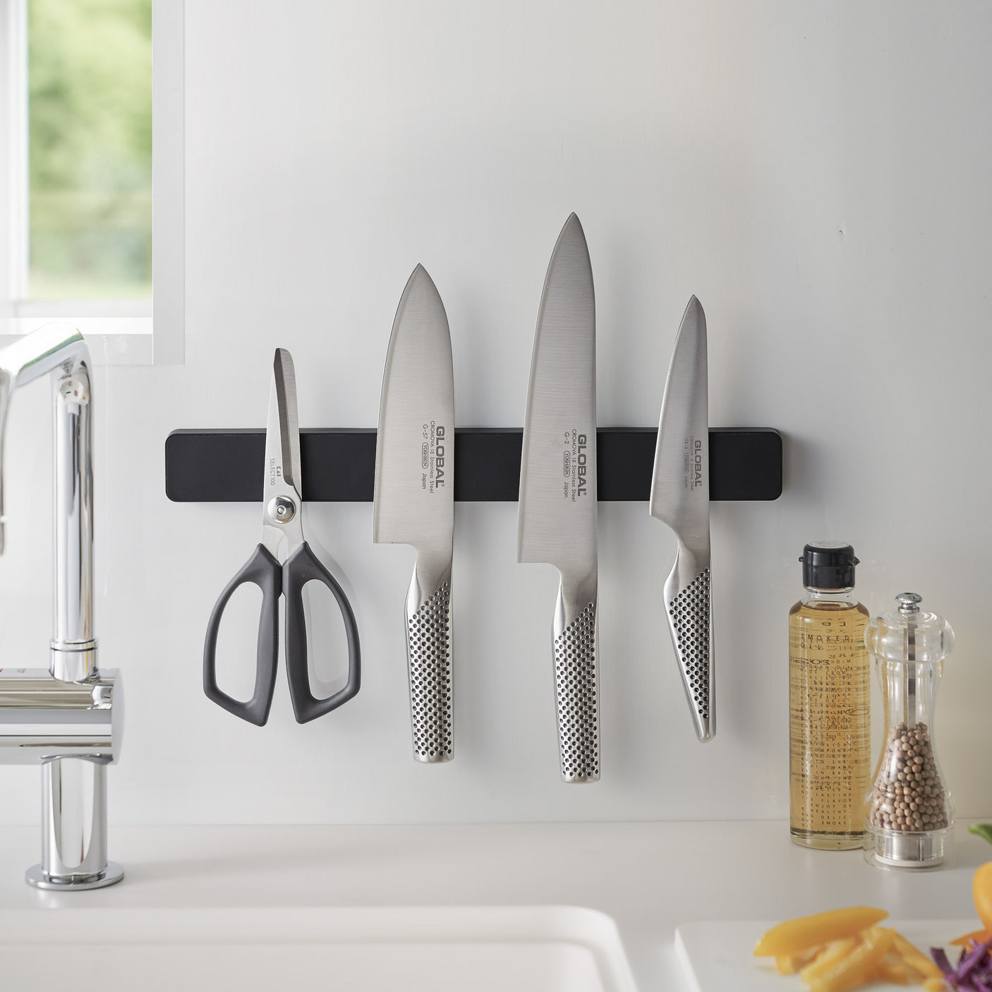 Flere kniver og redskaper hengende på sort magnetisk knivlist.