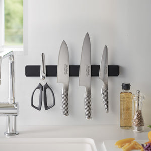 Flere kniver og redskaper hengende på sort magnetisk knivlist.