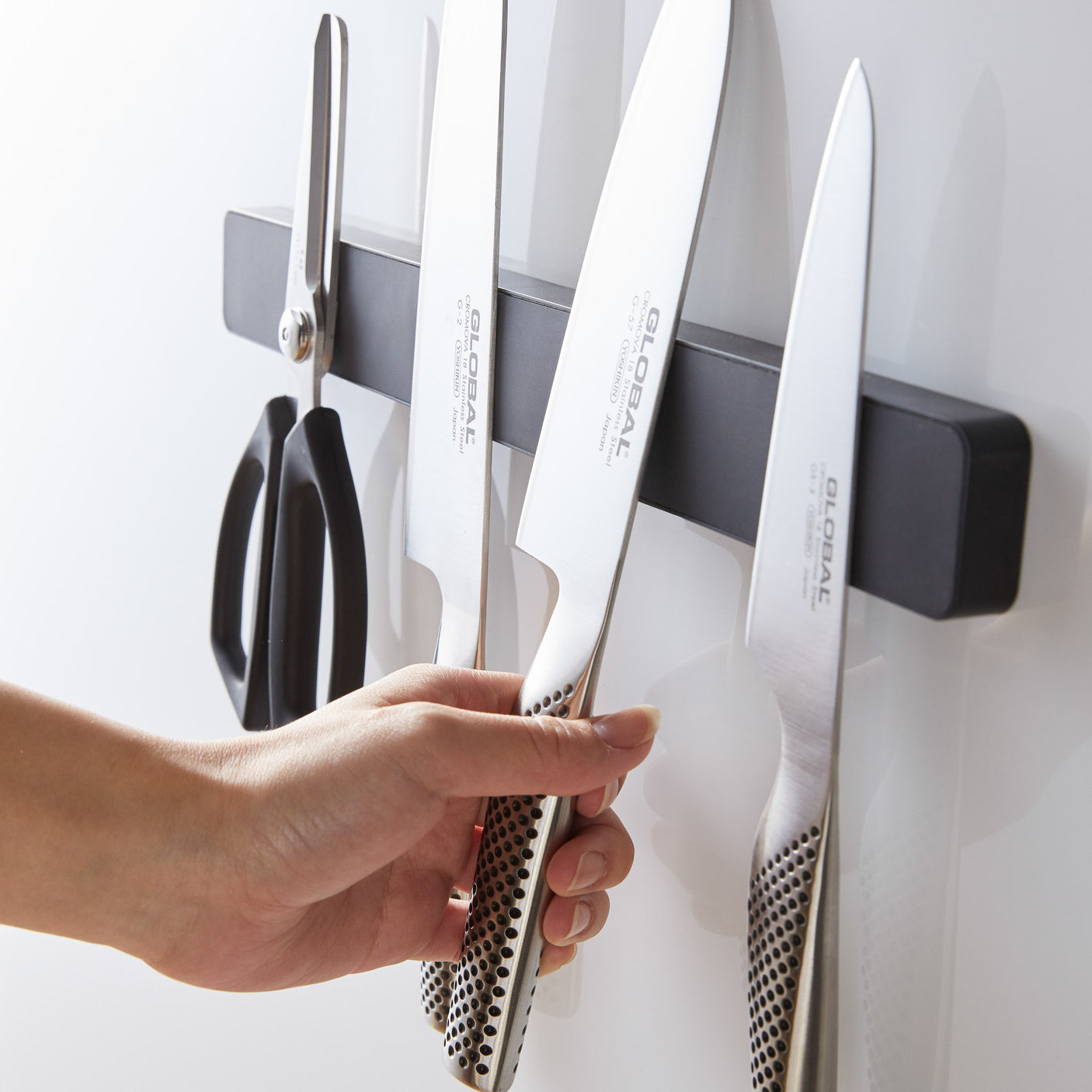 Hånd som fester kniv på sort magnetisk knivholder.