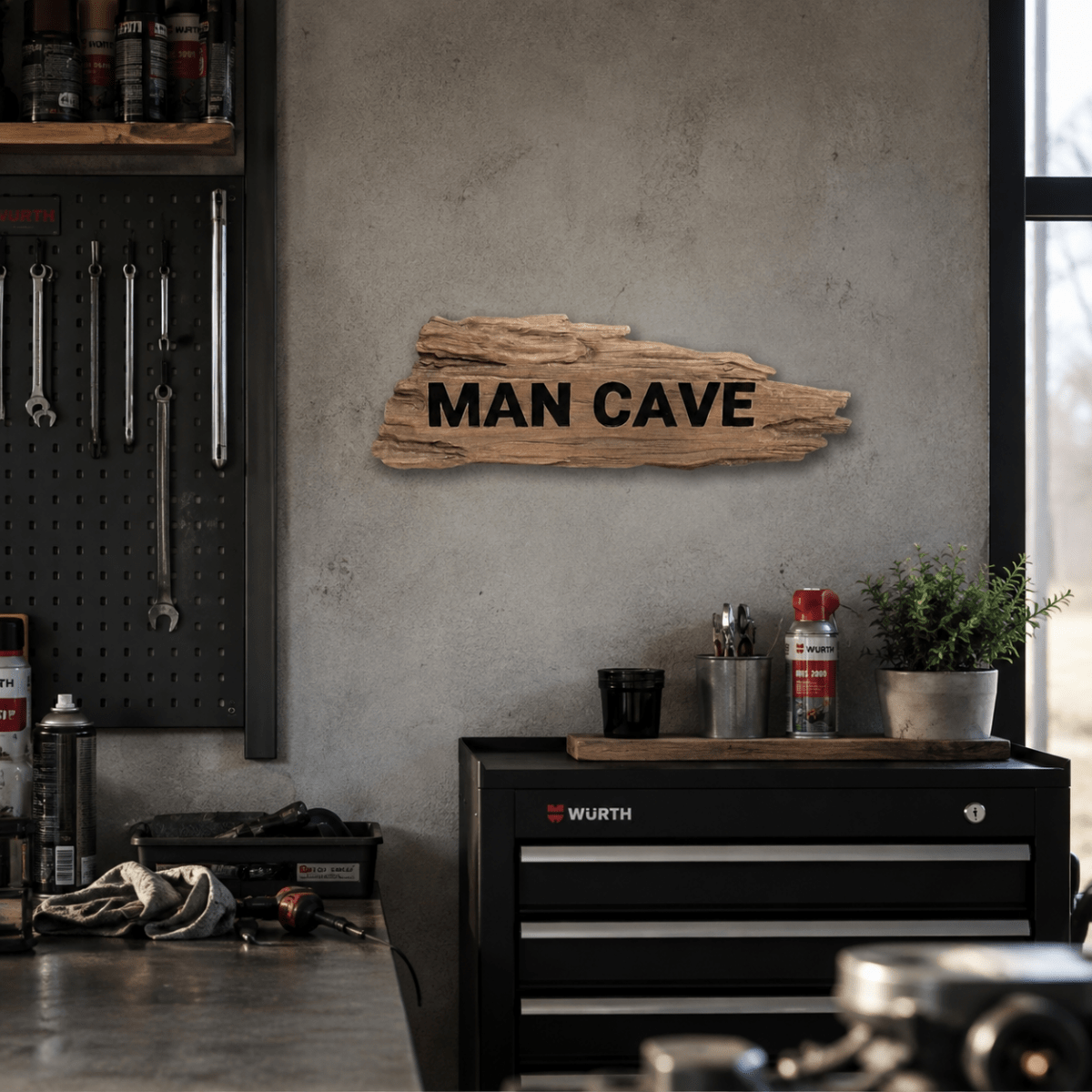 MAN CAVE veggskilt i tre montert på betongvegg over svart verktøyskap i moderne garasjeverksted.