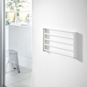 Hånd legger sammen hvit vegghylle i metall.