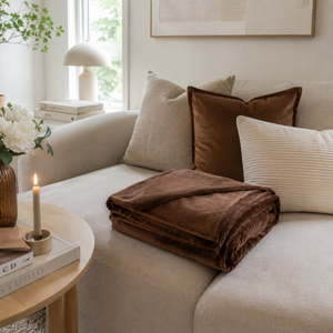 Mykt brunt flanellpledd 180 x 230 cm brettet på lys sofa