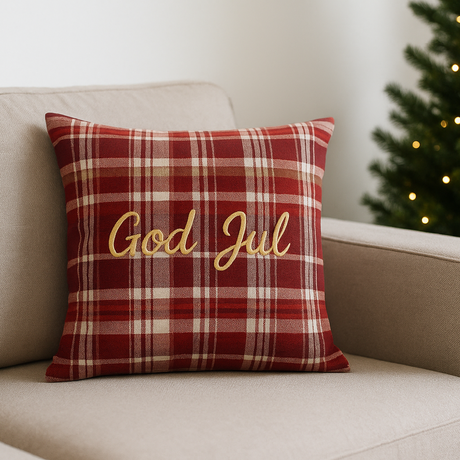 "Putetrekk i rødt rutemønster med teksten God Jul, plassert i beige sofa med juletre i bakgrunnen – klassisk julepynt til stue.