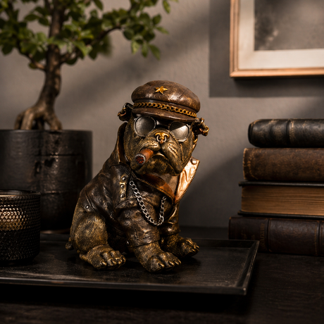 Bulldogfigur med hatt, solbriller, kjede og sigar plassert på trebord i rustikk stue med vase, bøker og varme fargetoner