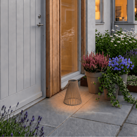 Brun solarlykt med varmt LED-lys plassert ved inngangspartiet til et moderne hus med blomster og grønne planter. - Lindas dekor