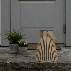 Brun solarlykt plassert ved et inngangsparti med grå dør, steinhelle og grønne planter i potter. - Lindas dekor