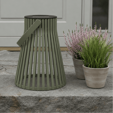 Grønn solarlykt plassert på en steinhelle ved et inngangsparti, med blomsterpotter i rosa og grønt ved siden av. - Lindas dekor 