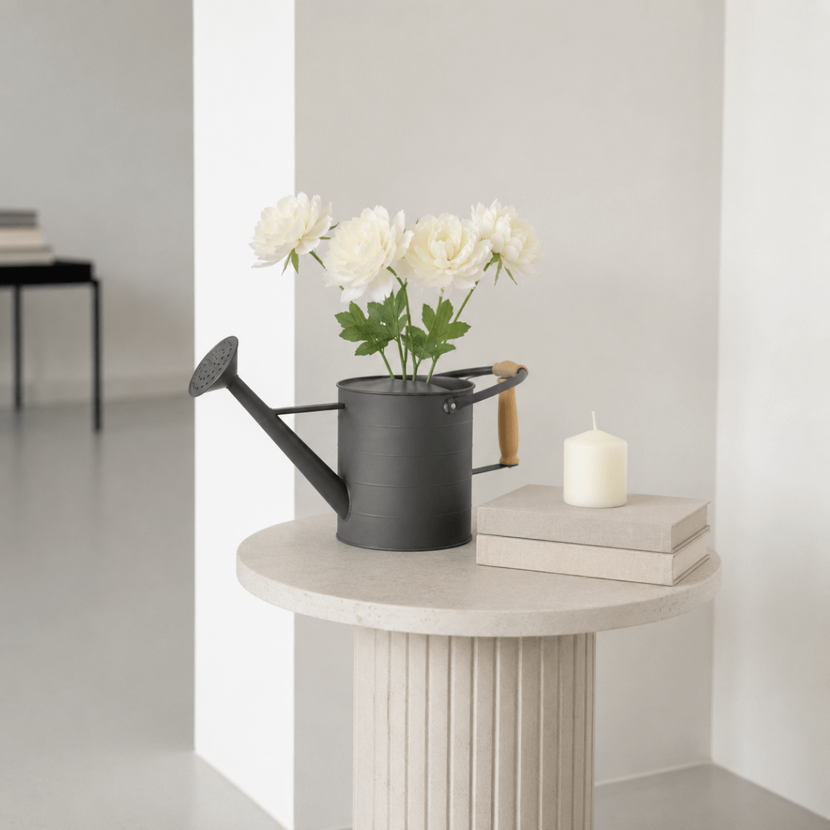 Mørk grå dekorativ vannkanne brukt som vase med hvite blomster på et rundt pyntebord i et lyst, nordisk interiør. - Lindas dekor 