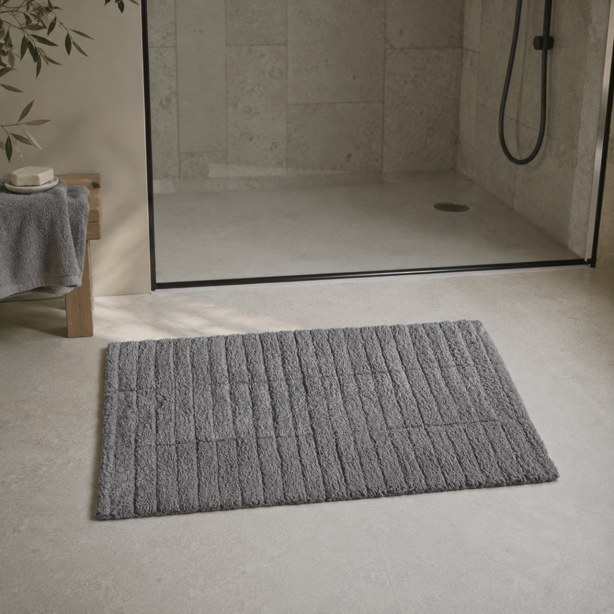 Grå Tiles baderomsmatte foran en dusj med glassvegg i et moderne baderom. - Lindas dekor