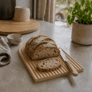 Rillet serveringsbrett i lyst bøketre med oppskåret brød og brødkniv på en lys kjøkkenbenk. - Lindas dekor 