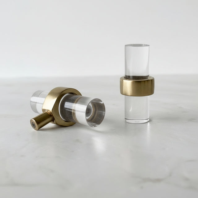 To Nesu T-bar knotter i glass og messing liggende på lys overflate.