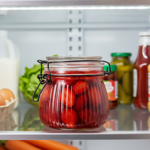 Glasskrukke med hengslet lokk fylt med syltede jordbær, plassert i kjøleskap – praktisk og dekorativ oppbevaring av mat.