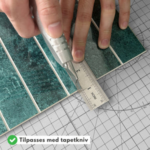 Hender som kutter Alma grønn marmorfliser til riktig størrelse med tapetkniv.