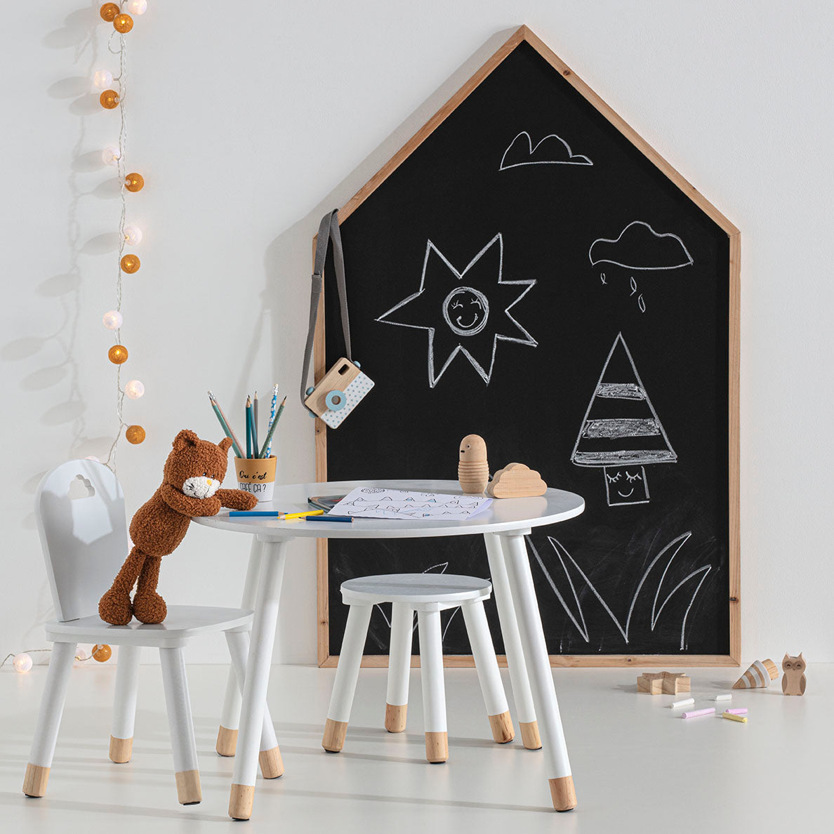 Husformet svart krittavle med kritttegninger i lyst og kreativt barnerom med lite bord og stoler.