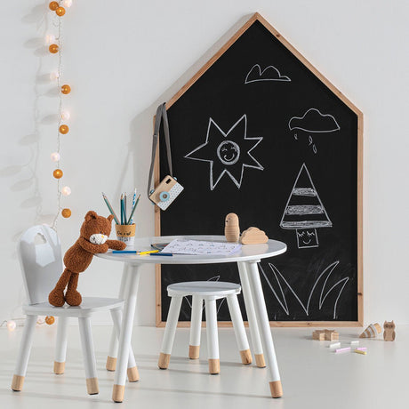 Husformet svart krittavle med kritttegninger i lyst og kreativt barnerom med lite bord og stoler.