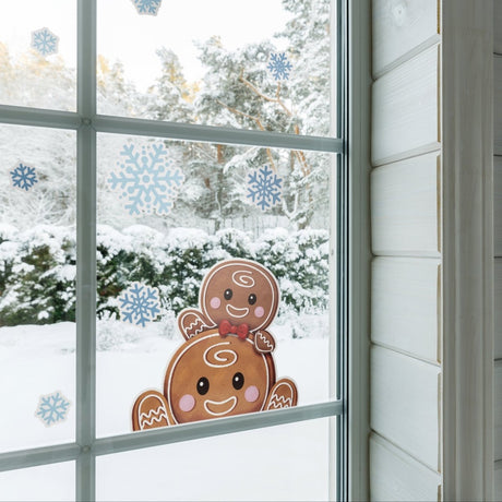 Vindu pyntet med pepperkakefigur-stickere og blå snøfnugg, snødekt skog utenfor