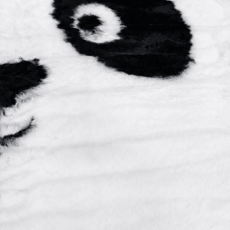Nærbilde av mykt pandateppe i svart og hvitt med fluffy overflate i polyester, designet som et pandaansikt til barnerom.