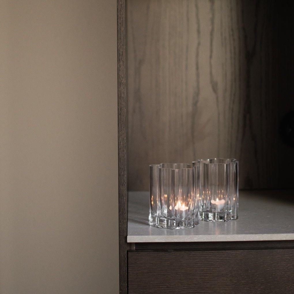 Flera klara ljuslyktor i flutad glas placerade på en mörk hylla med elegant kontrast.