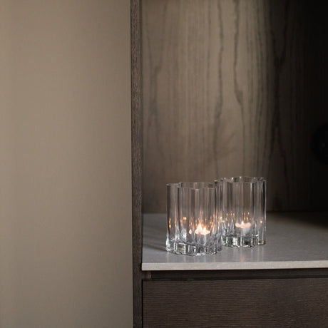 Flera klara ljuslyktor i flutad glas placerade på en mörk hylla med elegant kontrast.