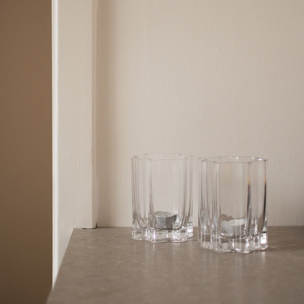 Två klara lyslykter i ribbad glas placerade på en ljus hylla i en lugn och modern inredning