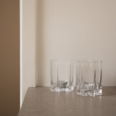 Två klara lyslykter i ribbad glas placerade på en ljus hylla i en lugn och modern inredning
