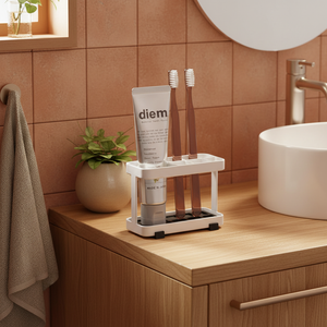 Hvit tannbørsteholder ved servant på bad med varme trefarger, grønne planter og naturlig lys i nordisk stil