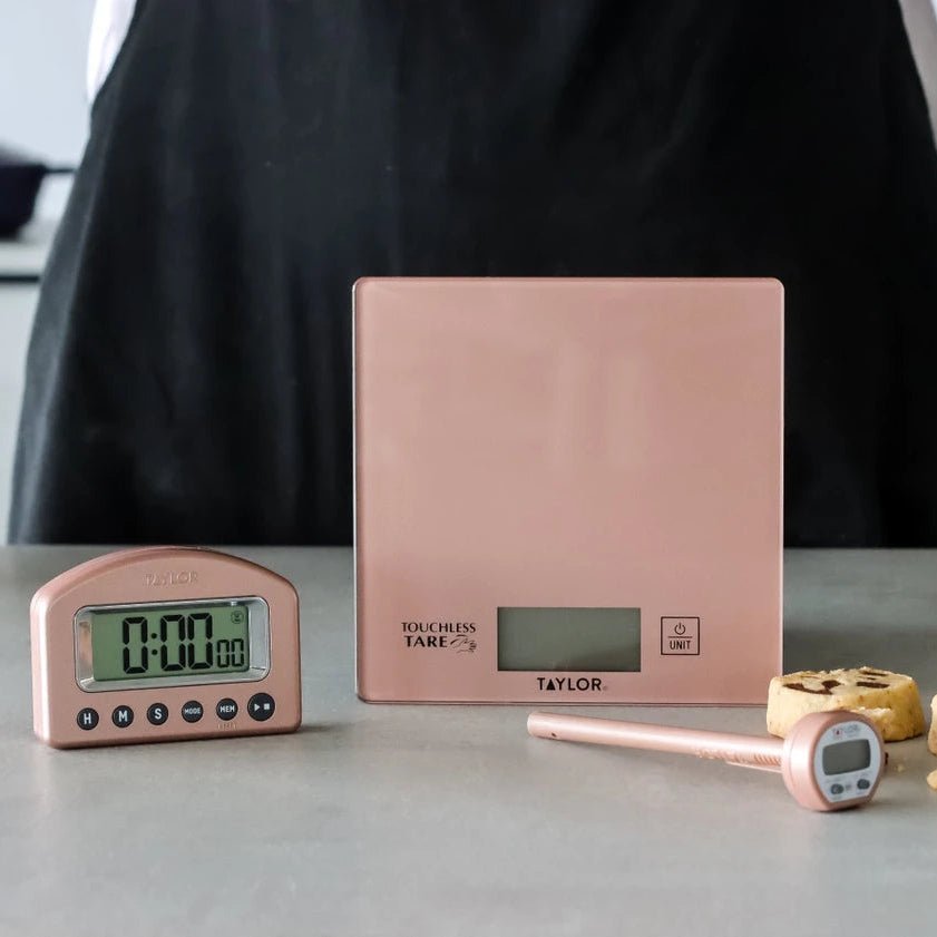 Kjøkkenvekt, timer og steketermometer i rosé i bruk under baking på kjøkkenbenken