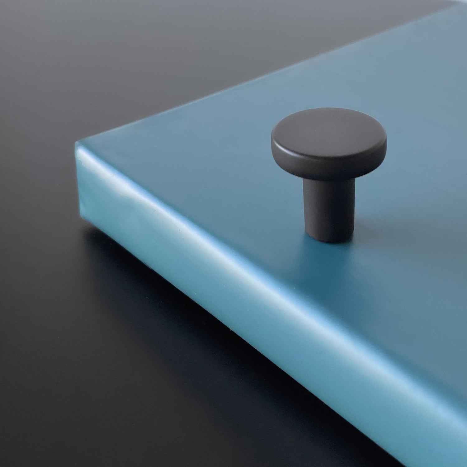 Sort moderne knott i matt metall montert på blå overflate, minimalistisk design.