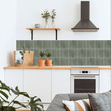 Selvklebende fliser i grønn finish montert over kjøkkenbenk i moderne interiør med tre og hvite detaljer.